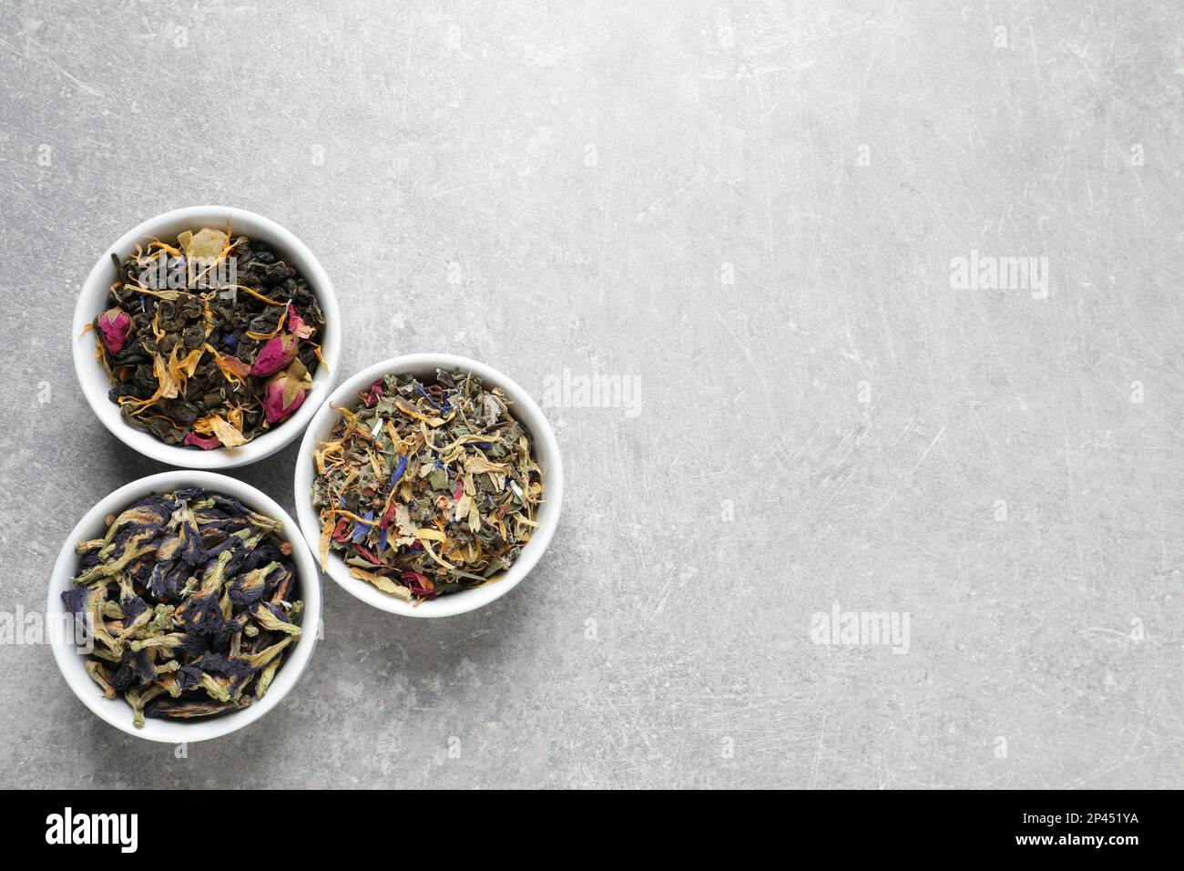 Flat lay composition with different dry teas on light grey table, space ...