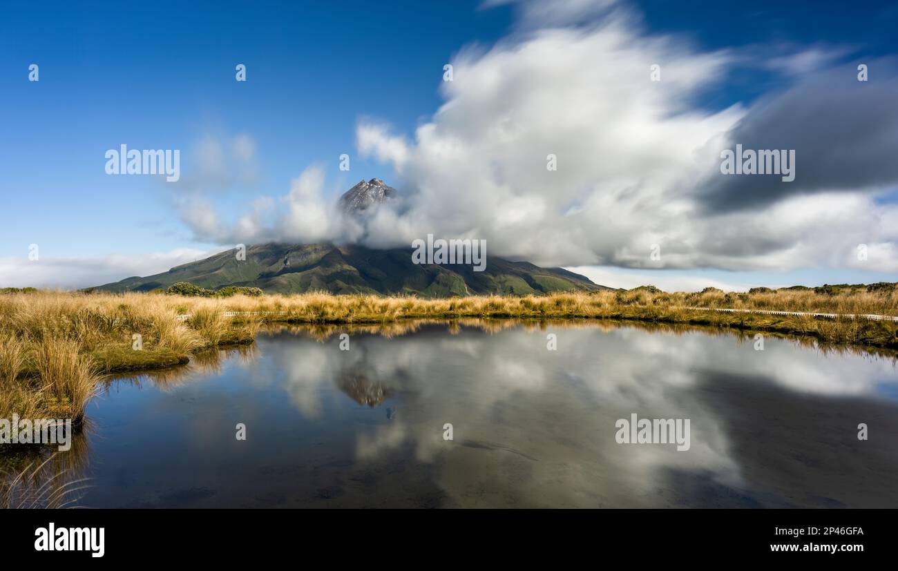 Mt Taranaki reflected in the Pouakai tarn. Clouds floating around the mountain peak. Taranaki. New Zealand. Stock Photo