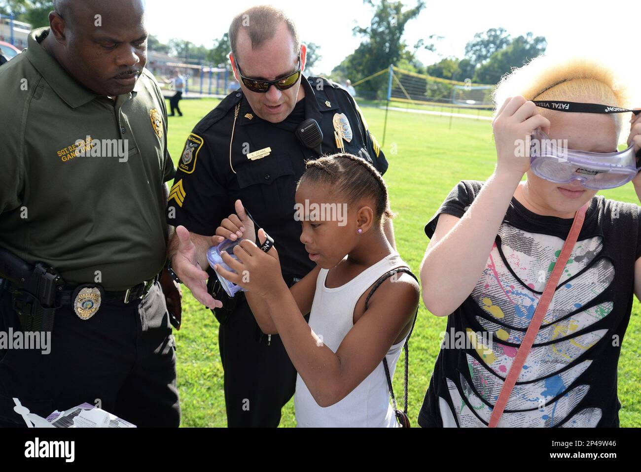 From left, Kinston Department of Public Safety Gang Unit Sgt. Dennis Taylor  and KDPS Sgt. Kevin Devine help K'deja Coward, 9, center, and Quanisia  Coward, 12, try out intoxication simulating goggles at, image size:1300x958