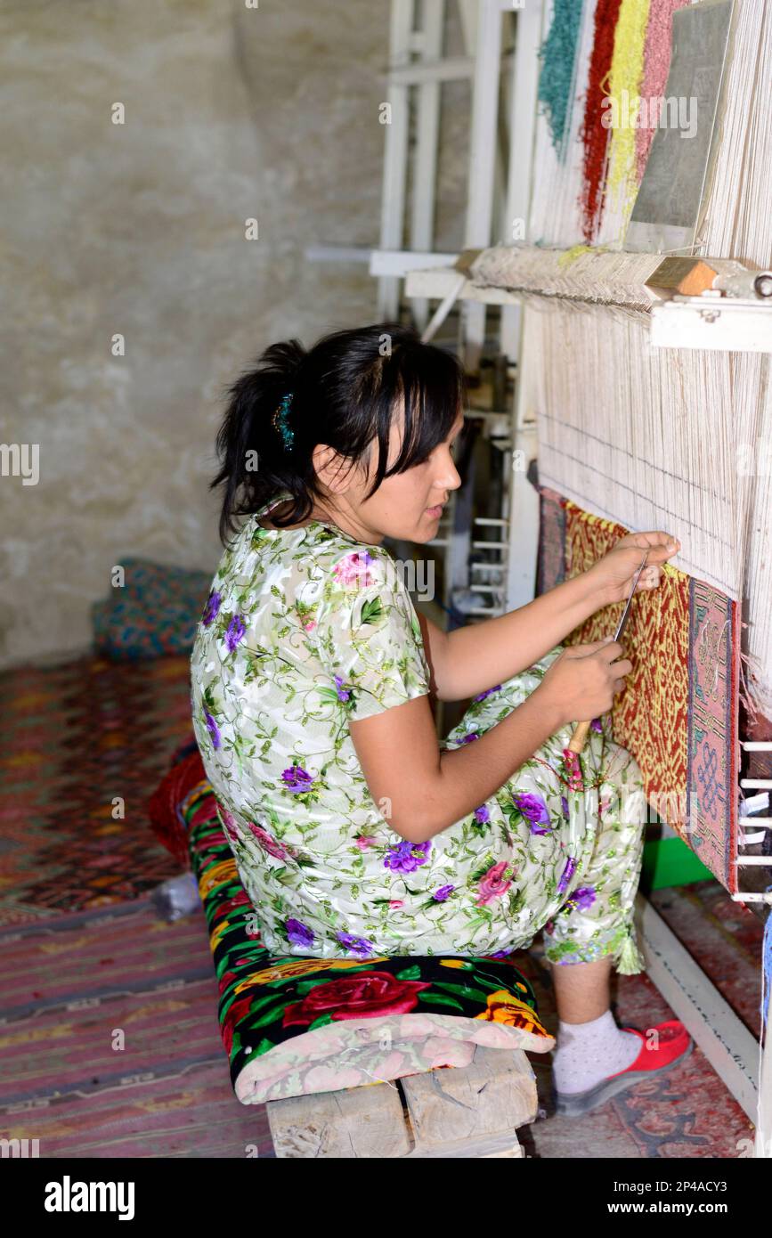 Uzbek women weaving a handmade traditional carpet in a small rug workshop in the old city of Bukhara, Uzbekistan. Stock Photo