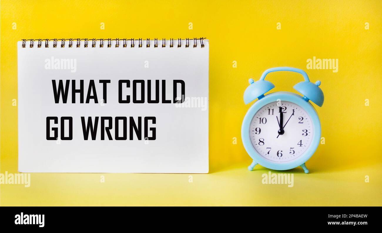 Top view of what can go wrong, text on notepad and yellow background with clock. Business concept. Stock Photo