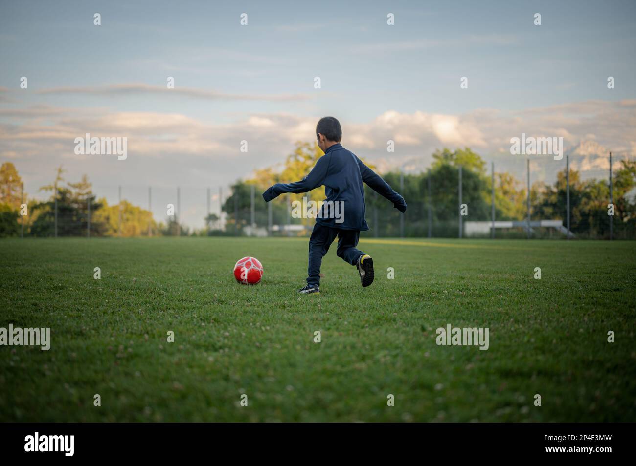 Child playing football. One Asian boy kicking the red ssoccer. Stock Photo