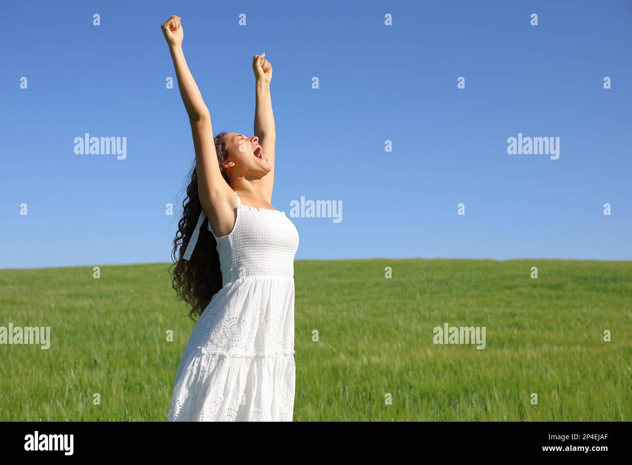 Excited woman in white dress raising arms and screaming in nature Stock Photo