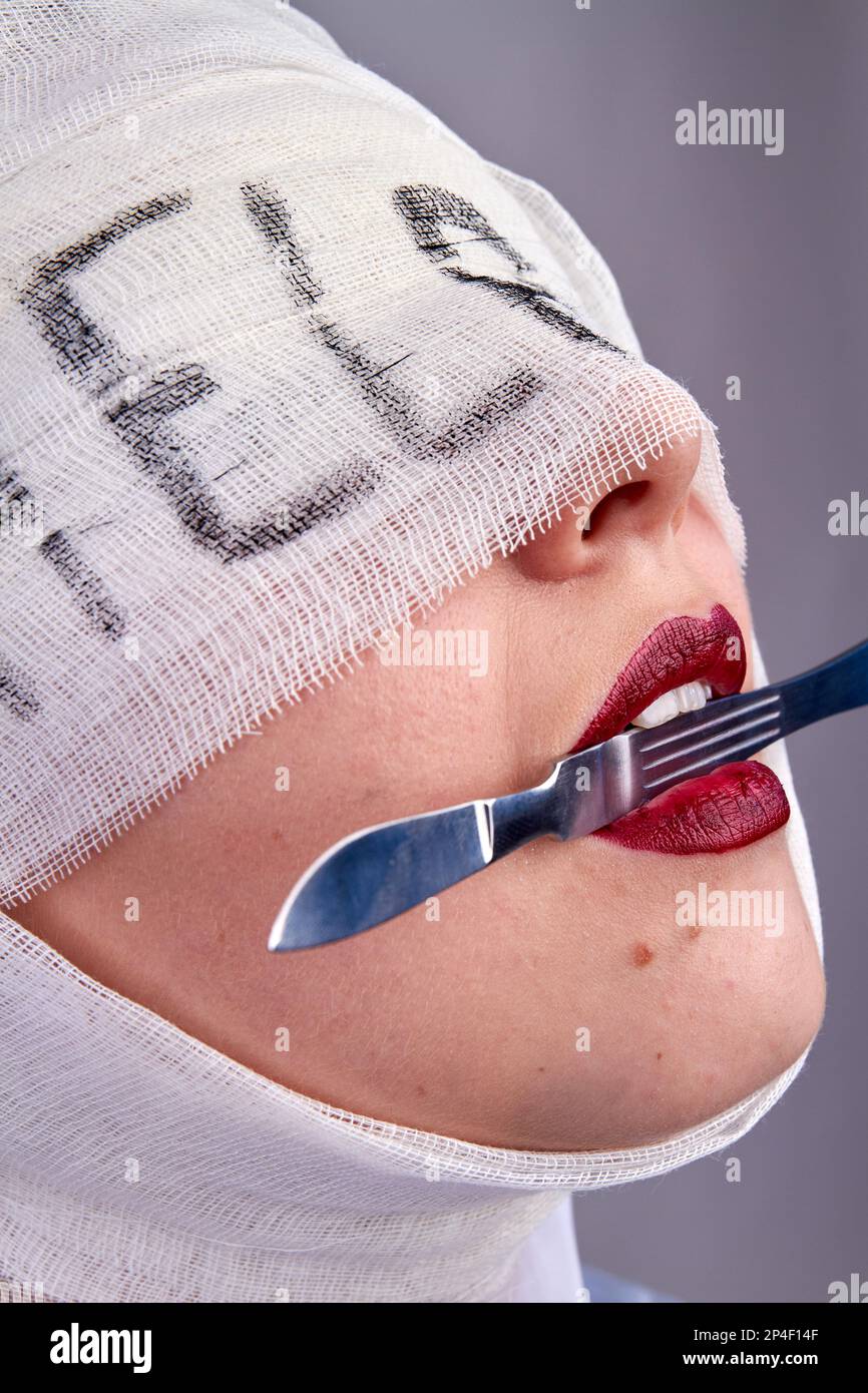 Close up womans face holding scalpel in her teeth. Bandaged head with
