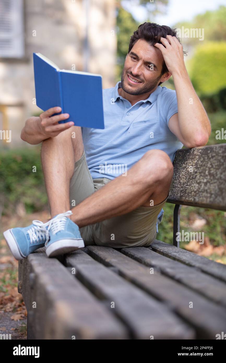 guy sitting on a bench in the park reading book Stock Photo - Alamy