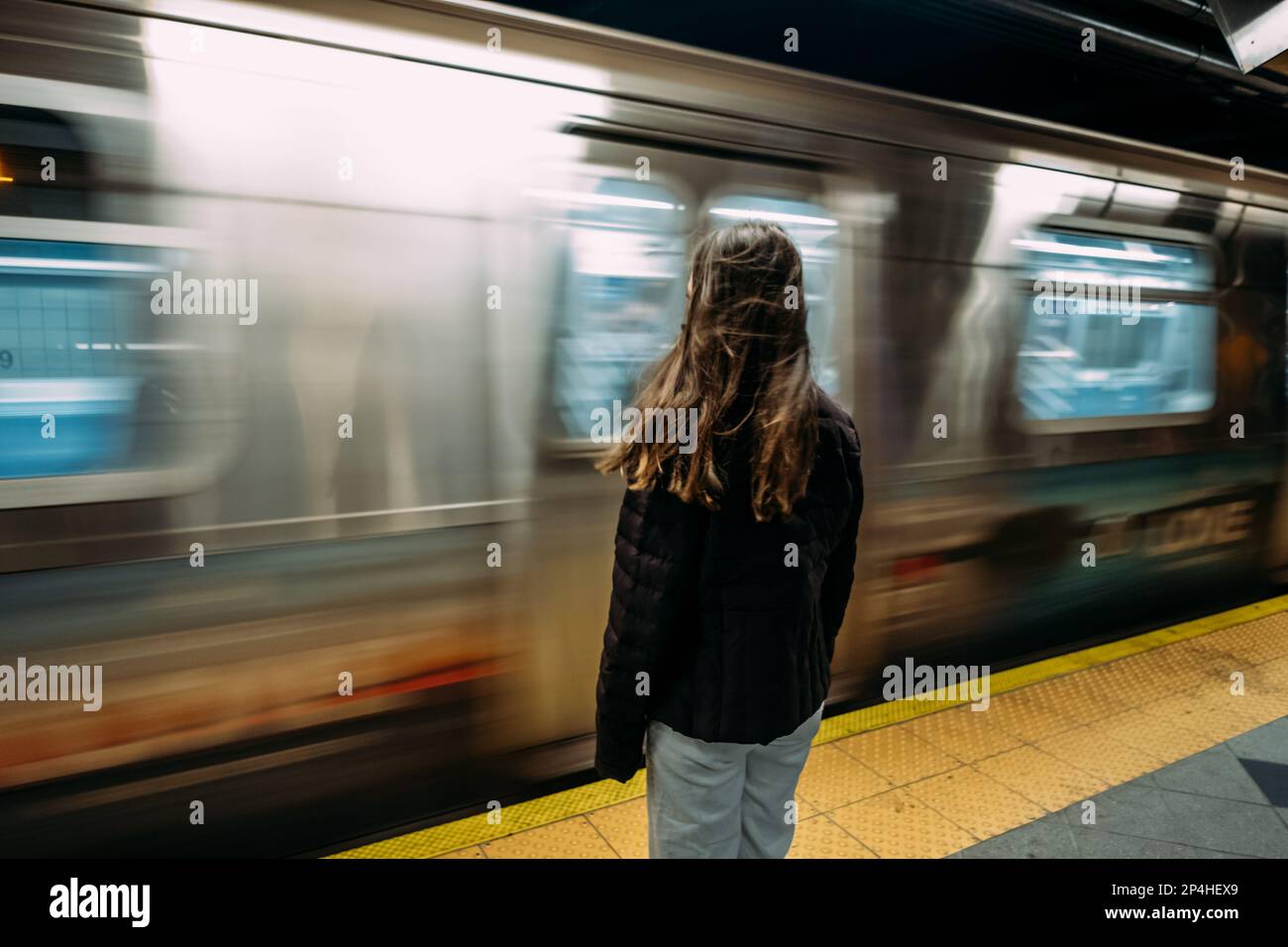 Teen girl standing in front of moving subway train Stock Photo