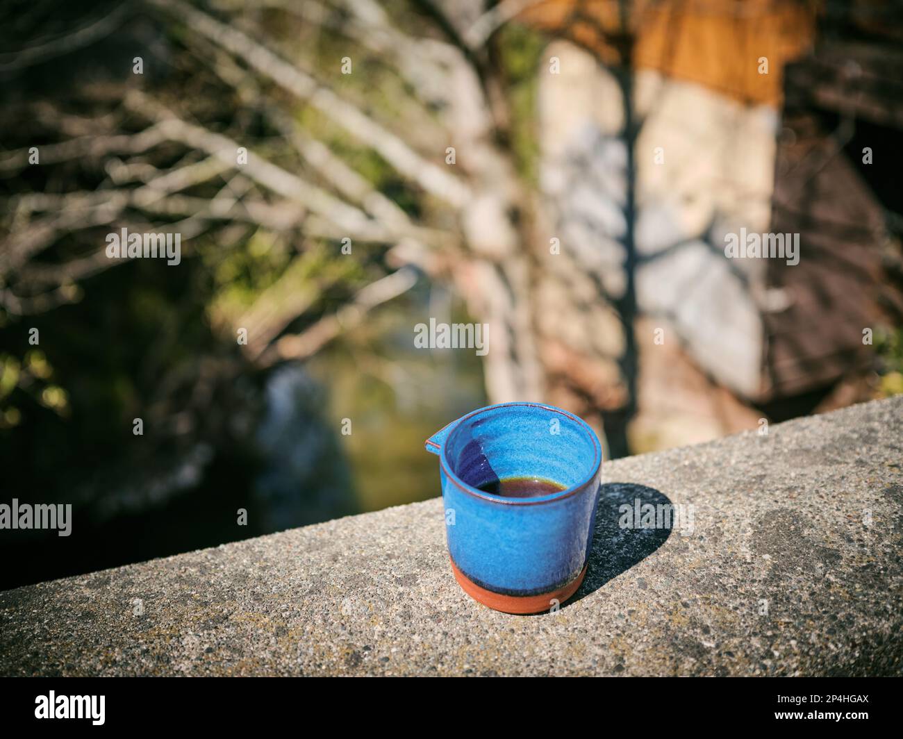 Half full blue ceramic coffee mug with unique handle outside on ledge Stock Photo
