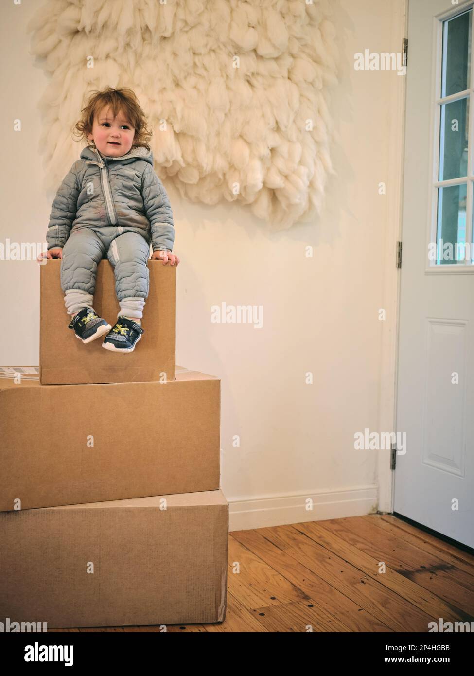 One year old sits on three cardboard boxes in family home Stock Photo