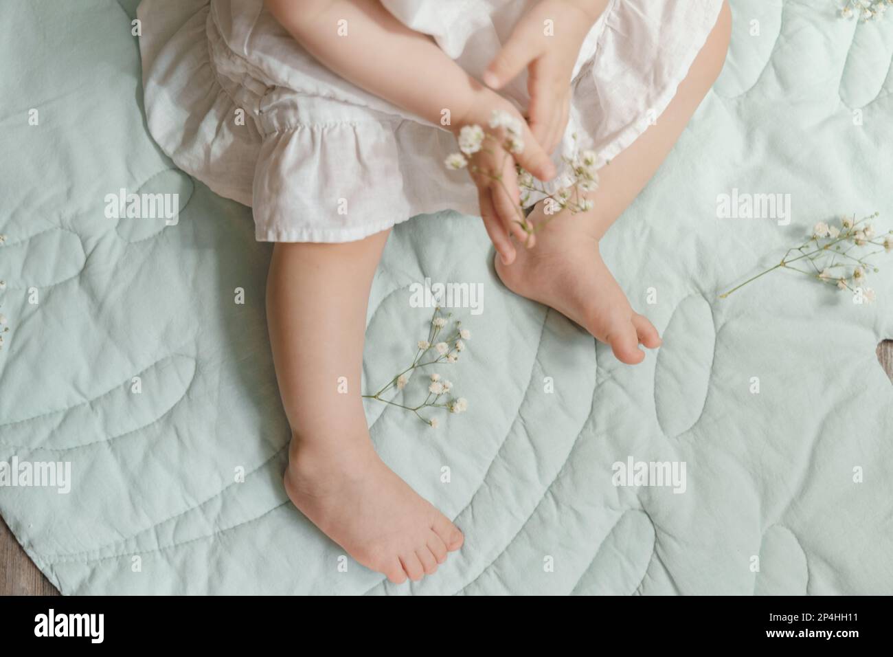 Hands and legs of a baby girl in a white linen dress with gypsophila Stock Photo