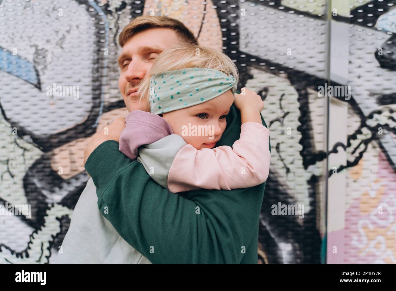 Dad in hoodie hugging little daughter in front of pastel graffiti Stock Photo