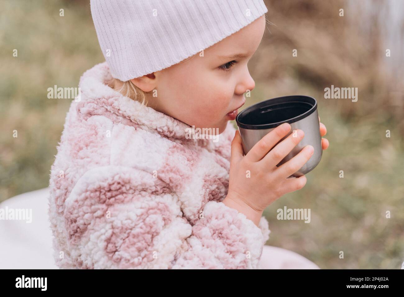 Baby girl drinking tea from a thermos near the river in late autumn Stock Photo