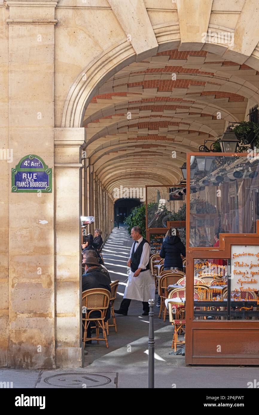 A waiter serving customers at Ma Bourgogne Restaurant in the arcade at Place Des Vosges in the Marais, Paris. Stock Photo