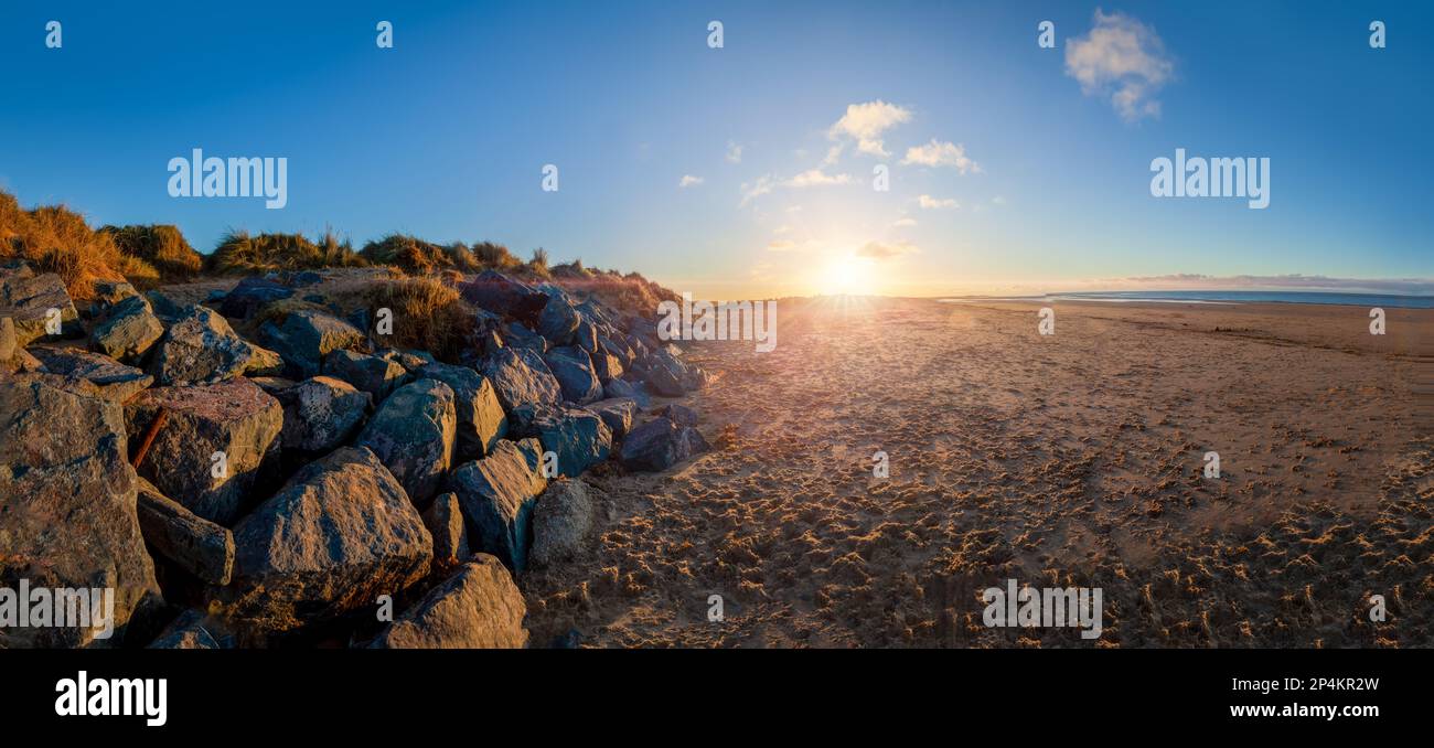 Stunning sunset at Brancaster beach with sand and sea defence rocks. Panoramic scenic landscape in North Norfolk Stock Photo