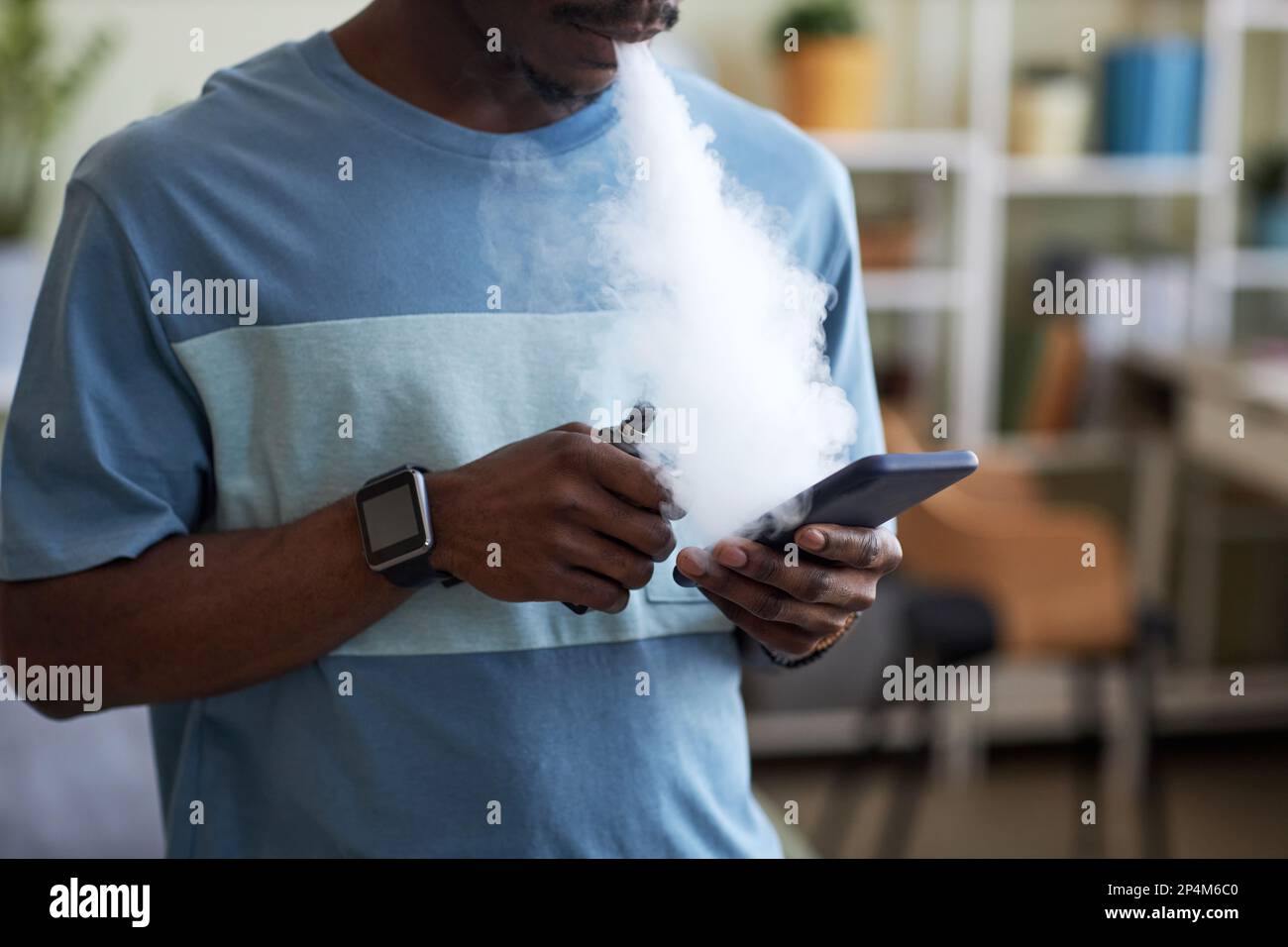 African American guy with e-cigarette in hand texting in smartphone and  releasing clouds of white thick vapor from his mouth Stock Photo - Alamy