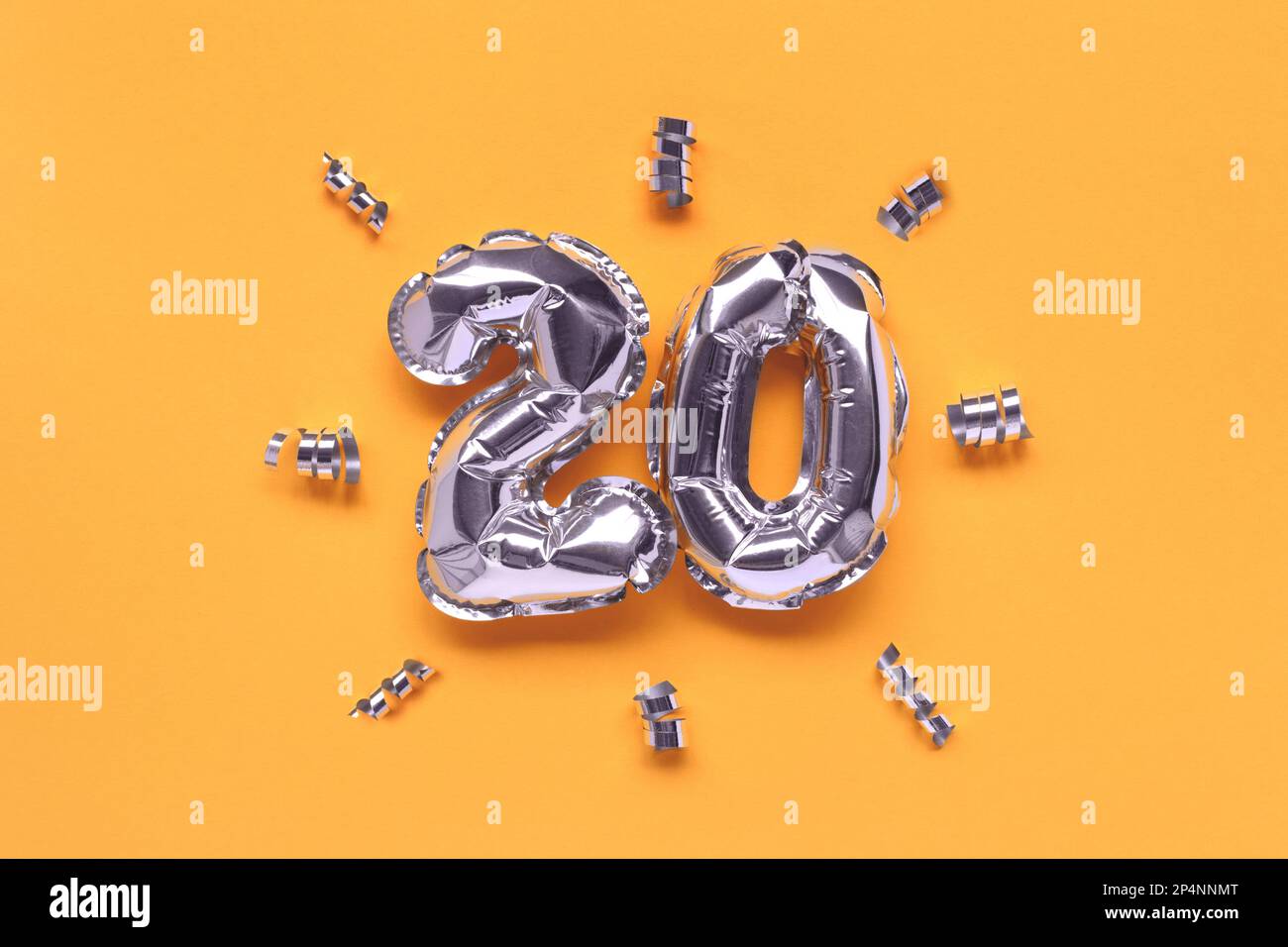 Number twenty silver balloons with ribbons confetti on a yellow background. Stock Photo
