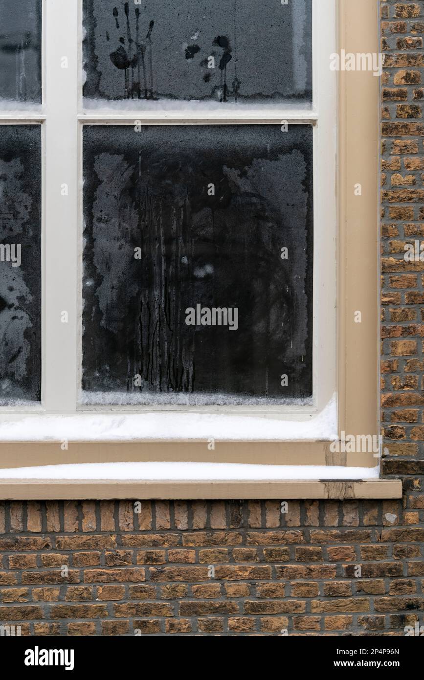 Facade of a dutch old brick house in Dordrecht, a frosty snowy dutch window in the winter, hand print, smudges and condensation on the glass. Stock Photo
