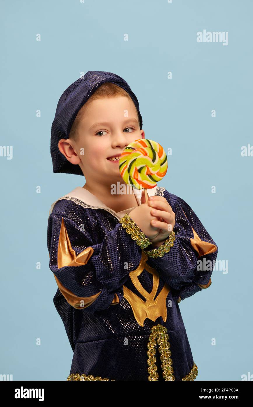 Cute little charming boy in costume of medieval pageboy, little prince with big lollipop over