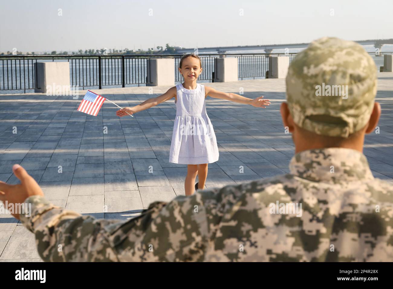 Little girl with flag of USA running towards her father in military uniform outdoors. Family reunion Stock Photo