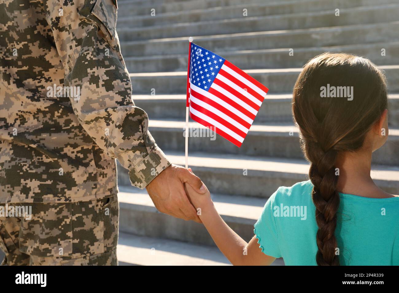 Soldier and his little daughter with American flag holding hands outdoors, back view. Veterans Day in USA Stock Photo