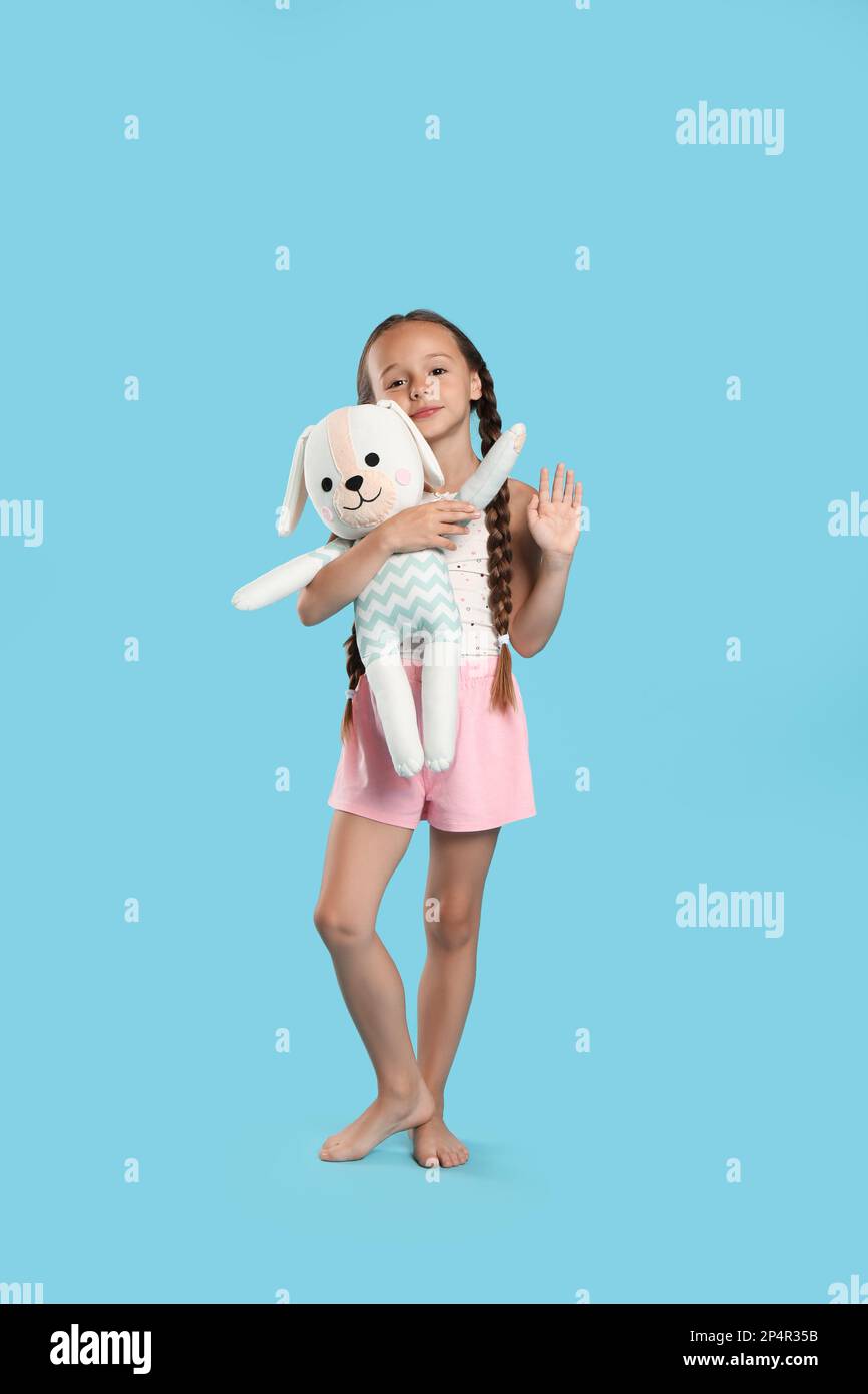 Cute girl wearing pajamas with toy on light blue background Stock Photo ...