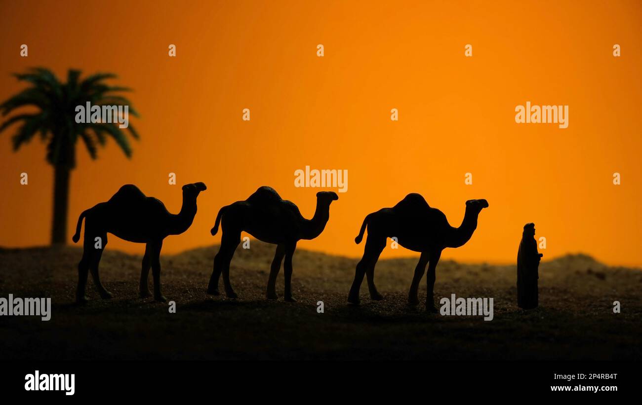 Miniature people toy figure photography. Silhouette of middle eastern man walking with camels in desert at sunset dawn time. Image photo Stock Photo
