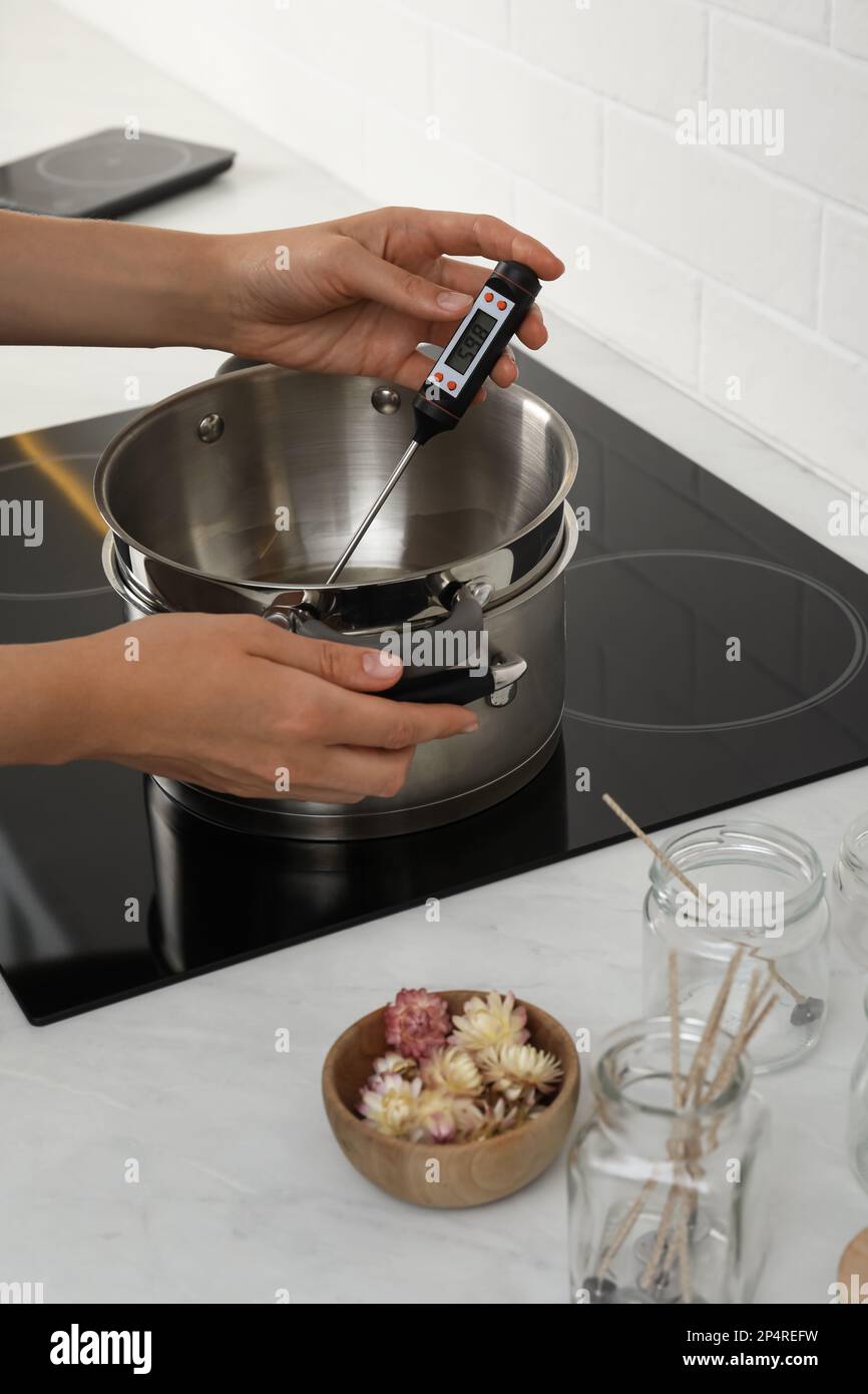 Woman measuring temperature of melted wax in kitchen, closeup. Making