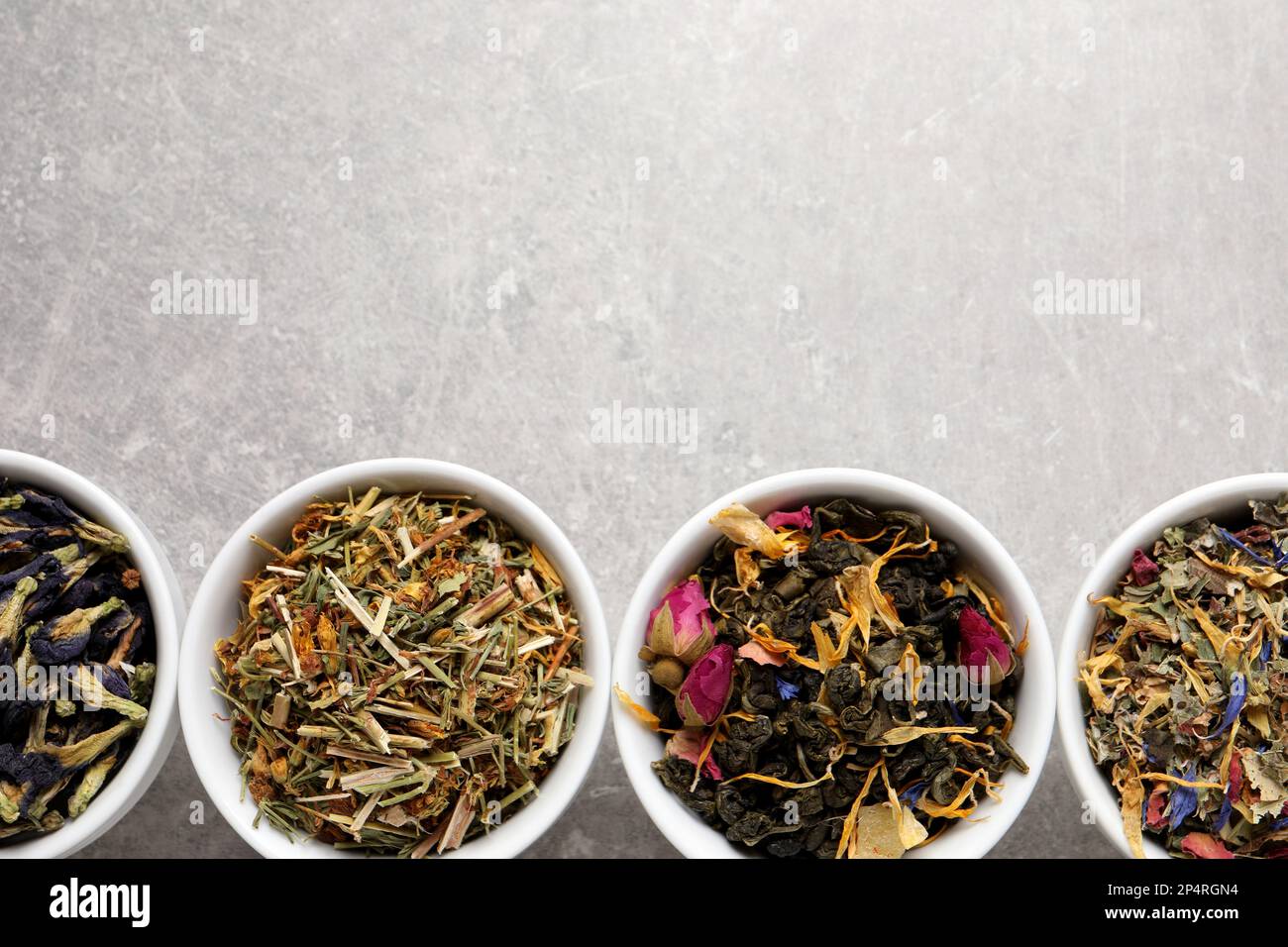 Flat lay composition with different dry teas on light grey table, space ...
