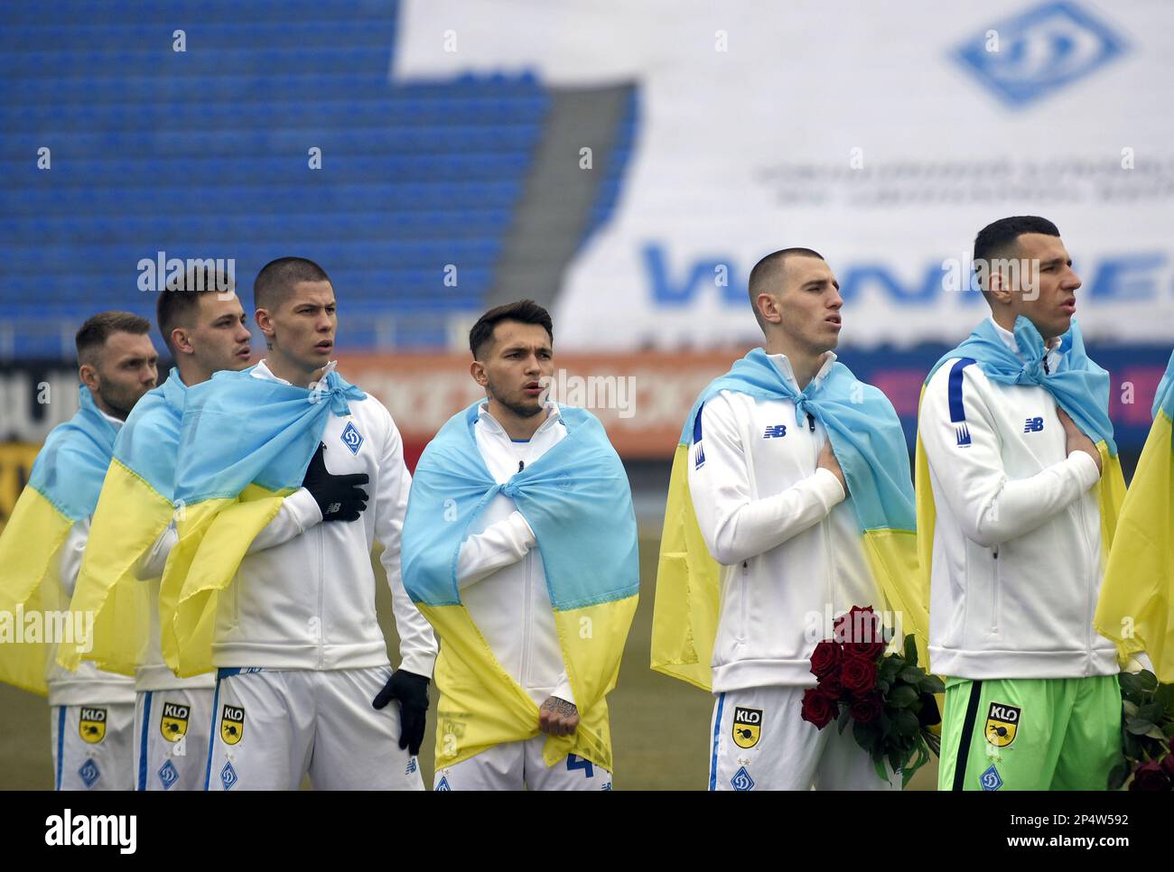 KYIV, UKRAINE - MARCH 4, 2023 - Players of FC Dynamo Kyiv wrapped in Ukrainian flags perform the national anthem before the 2022-2023 Ukrainian Premie Stock Photo