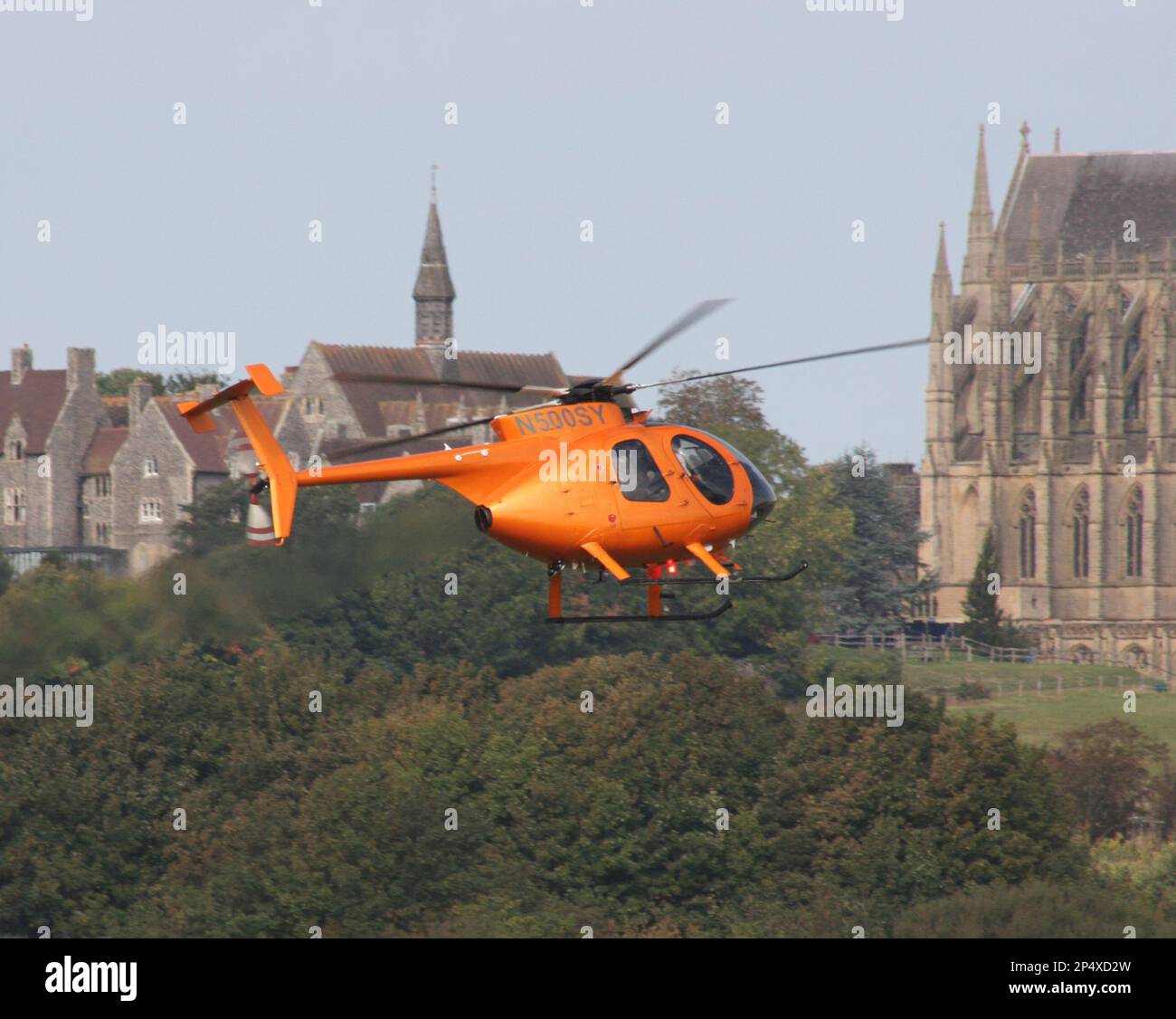 A McDonnell Douglas MD-500E helicopter takes off at Brighton City Airport. Lancing College to the rear Stock Photo