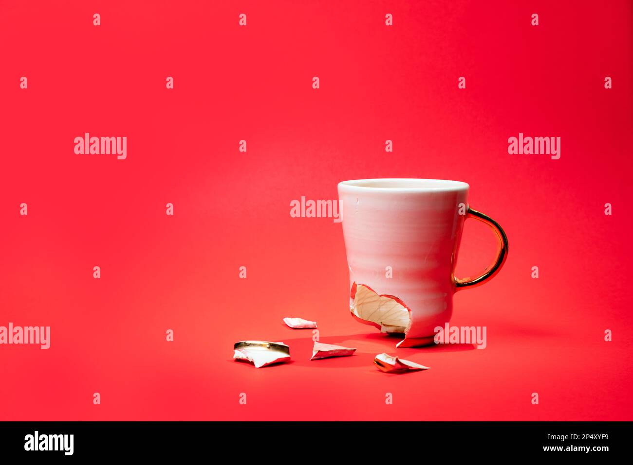 Broken tea cup isolated on red background. Cracked coffee mug and fragile ceramic pieces Stock Photo