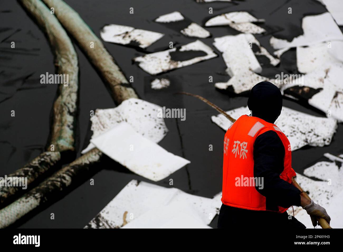 A worker clears oil floating on the sea after a pipeline explosion in
