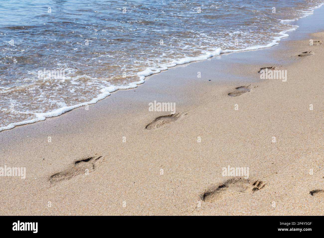 Footprints of a man on the yellow beach sand from walking barefoot by the sea with water that washes away the footprints. Contemplation of life Stock Photo