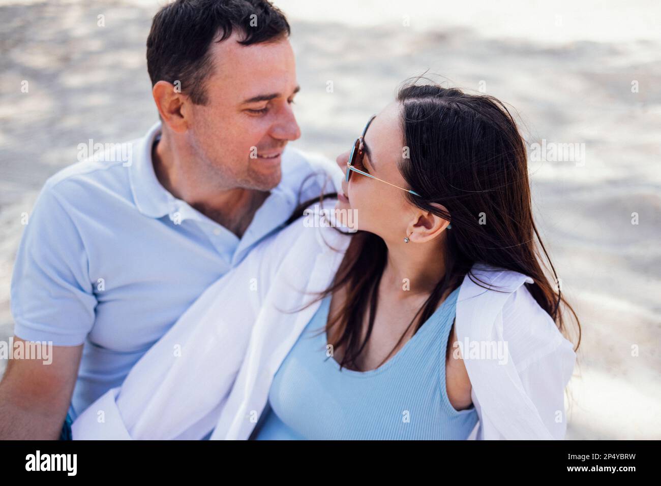 Caucasian couple in love on a sandy beach. Young man lovingly looks at a  beautiful woman in sunglasses. Girlfriend and boyfriend smile at each other  Stock Photo - Alamy
