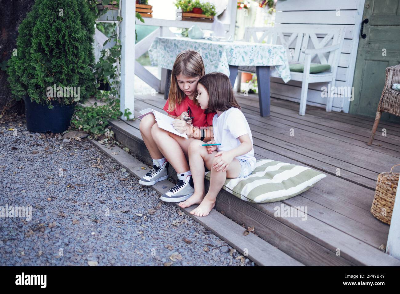 Two little girls are sitting on the pillows on the wooden floor of the ...