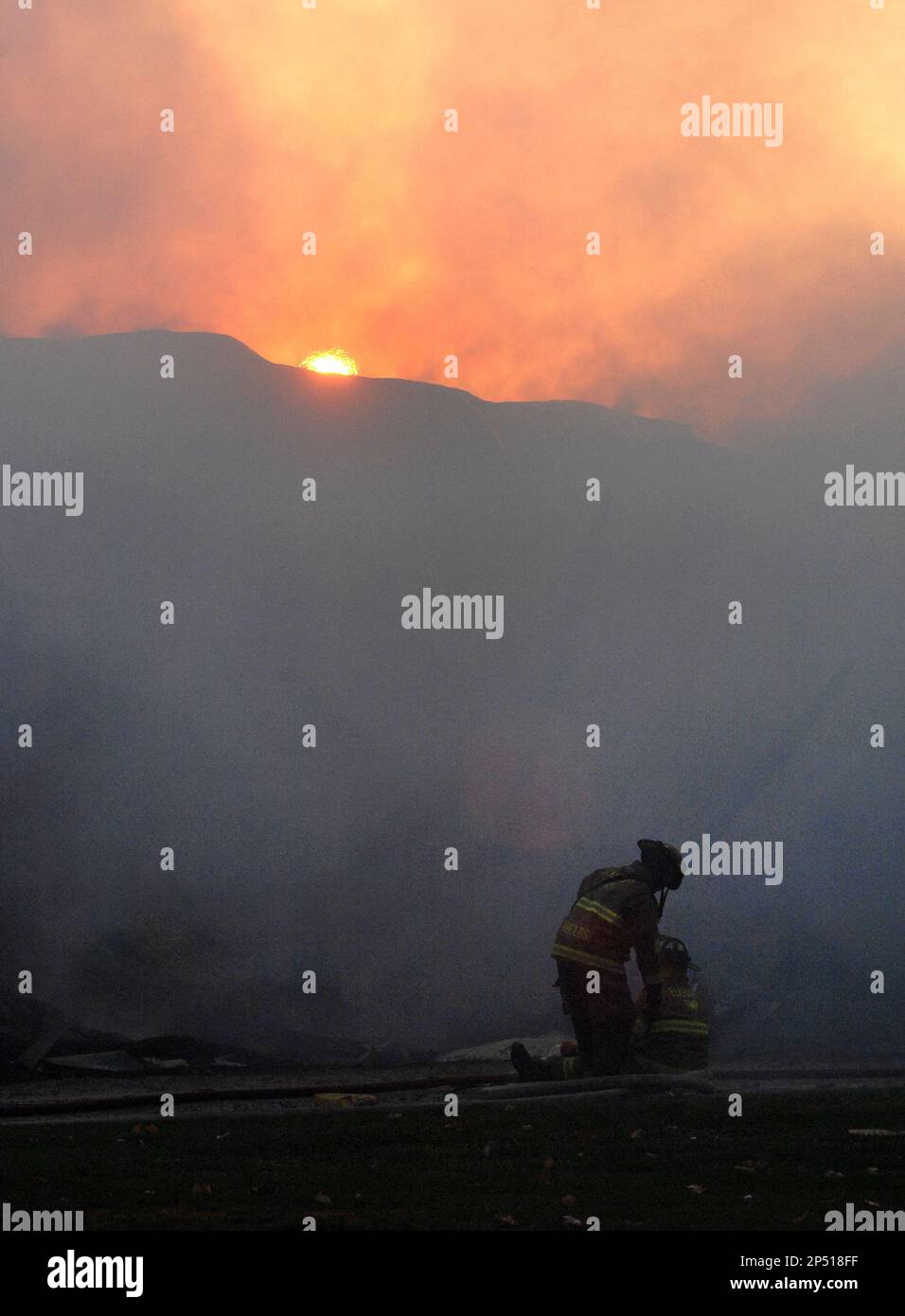 Firefighters spray water on the smoldering wood pile and remains of a