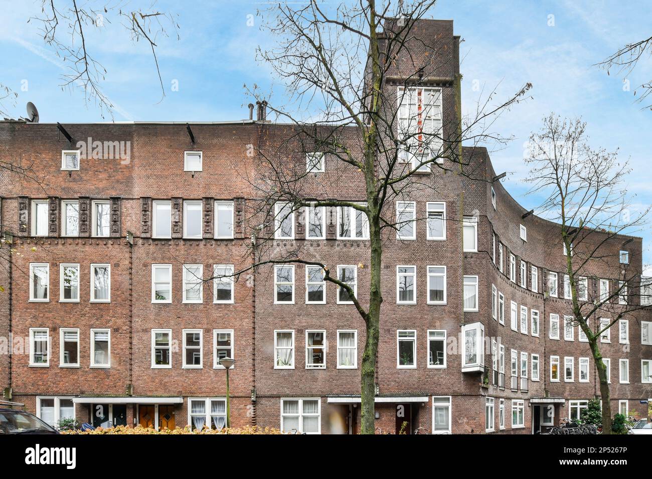 Amsterdam, Netherlands - 10 April, 2021: an apartment building with cars parked on the street next to it and a clock tower in the top right corner Stock Photo