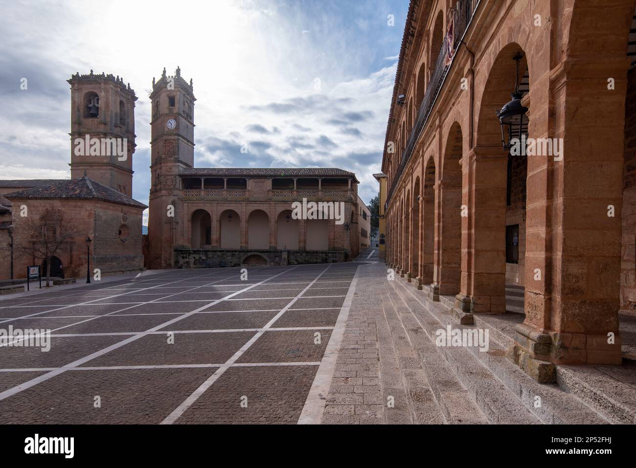 Square with a cobblestone floor, with a side with arches and in the background a church next to another building. Stock Photo