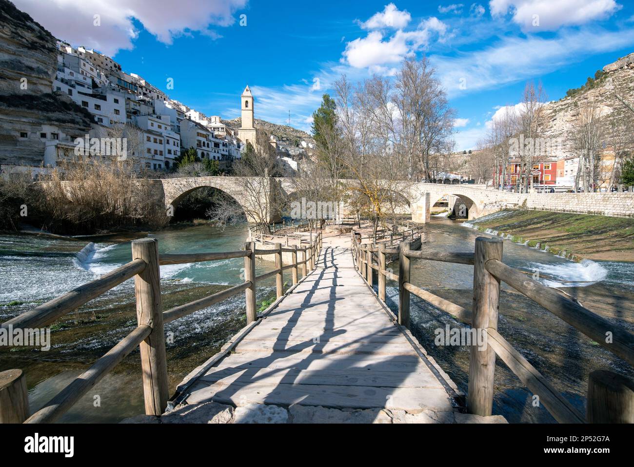 River flowing over a bridge leading to a mountain village and a blue sky with white clouds. Stock Photo
