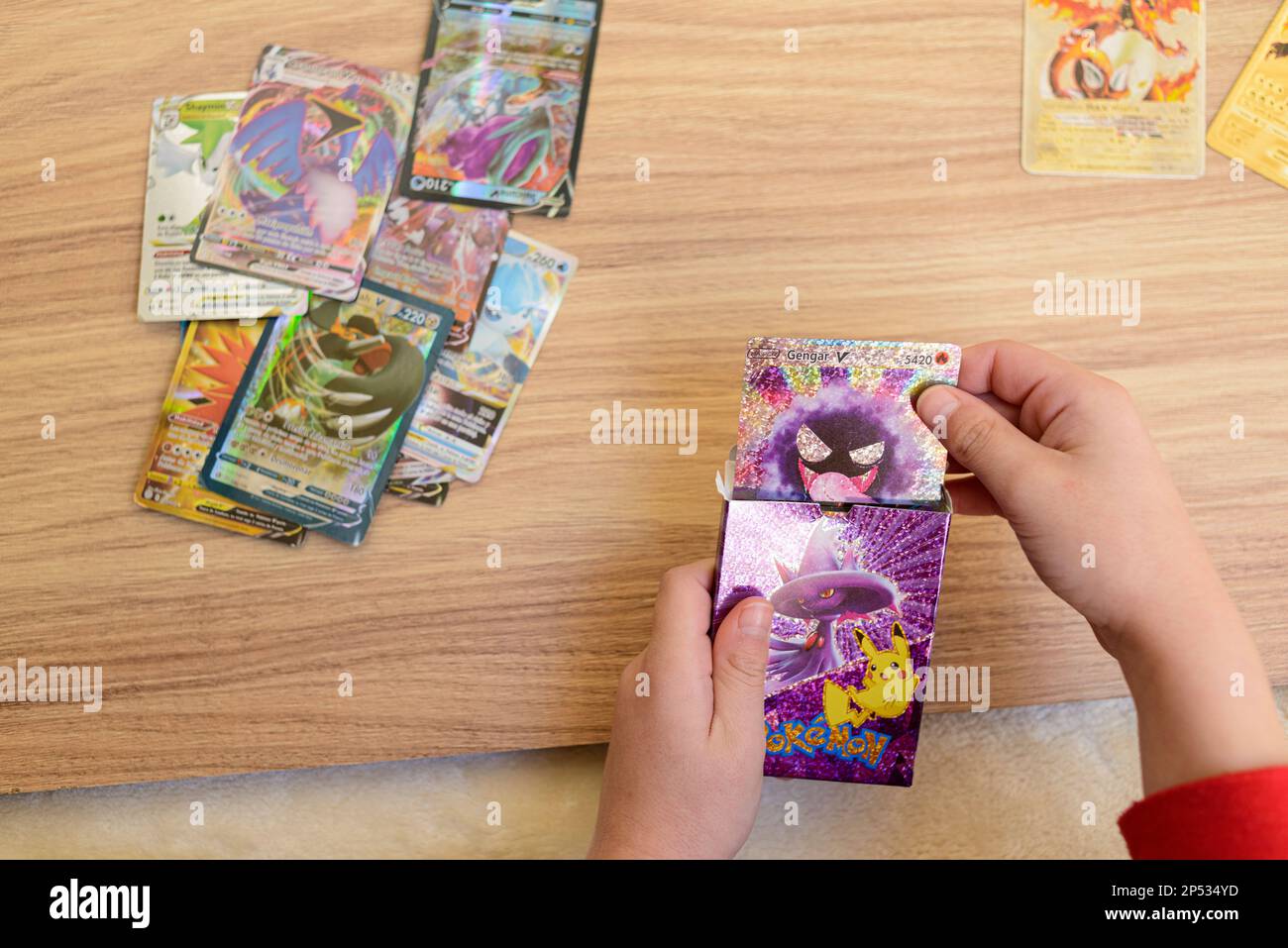 Arahal. Seville. Spain. 1st March 2023. Detail of a child's hands placing rare collectible Pokemon trading cards on a wooden table. Collectible tradin Stock Photo