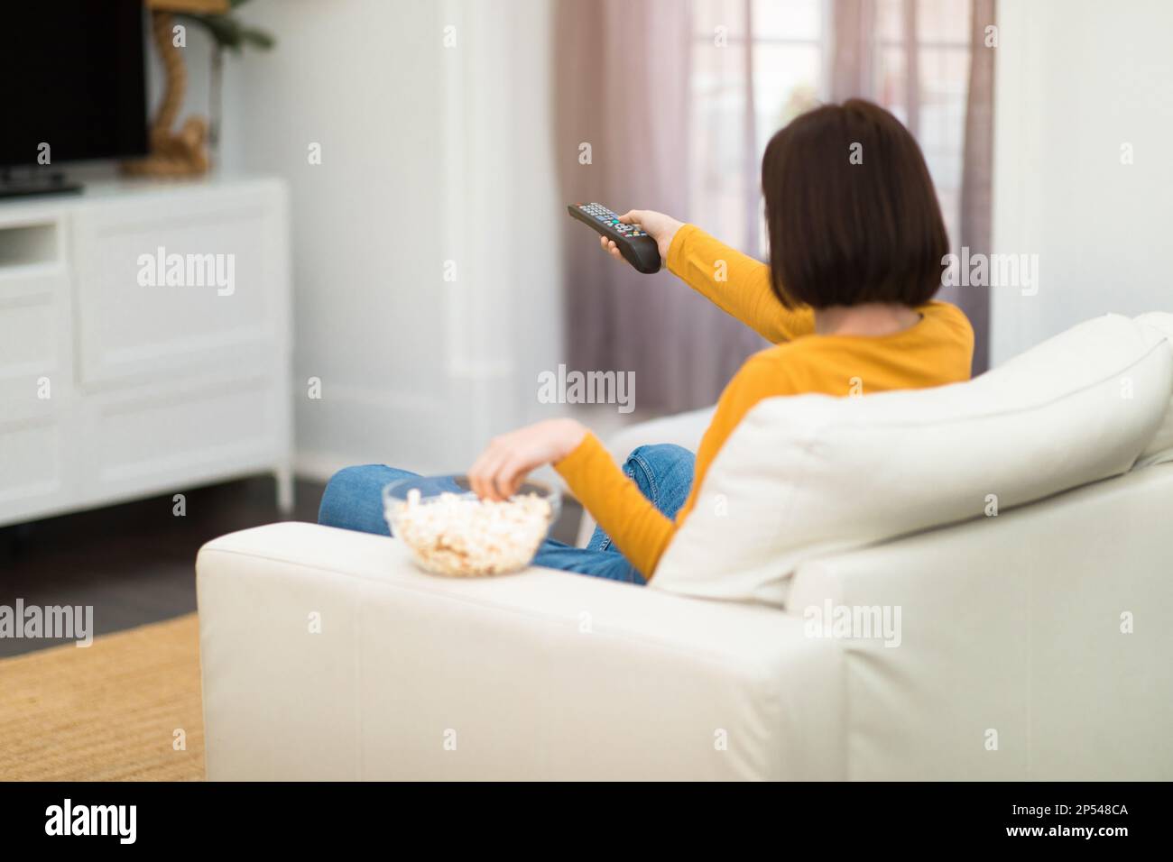 Back view of brunette woman switching channels on TV Stock Photo