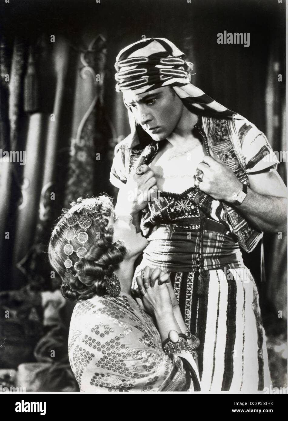 1926 , USA : The silent screen movie actor RUDOLPH VALENTINO ( born Rodolfo Guglielmi , 1895 - 1926 ) with WILMA BANKY in THE SON OF THE SHEIK ( Il figlio dello Sceicco ) by George Fitzmaurice , from the novel by Edith Maude Hull , Paramount Picture . - CINEMA MUTO - RODOLFO - attore cinematografico - VILMA - LATIN LOVER - italoamericano - italo americano - italo-americano - emigrant - emigrante - italo-american - portrait - ritratto - turbante - turban - arab - arabo - abbraccio - embrace - kiss - bacio - innamorati - lovers - amanti - ascella - ascelle - armpits - curls - boccoli - riccioli Stock Photo