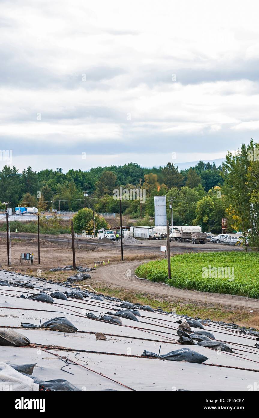 Weighted plastic sheeting covers a hillside in an active landfill.  Probably PVC geomembranes in the foreground, a landfill facility in the distance. Stock Photo