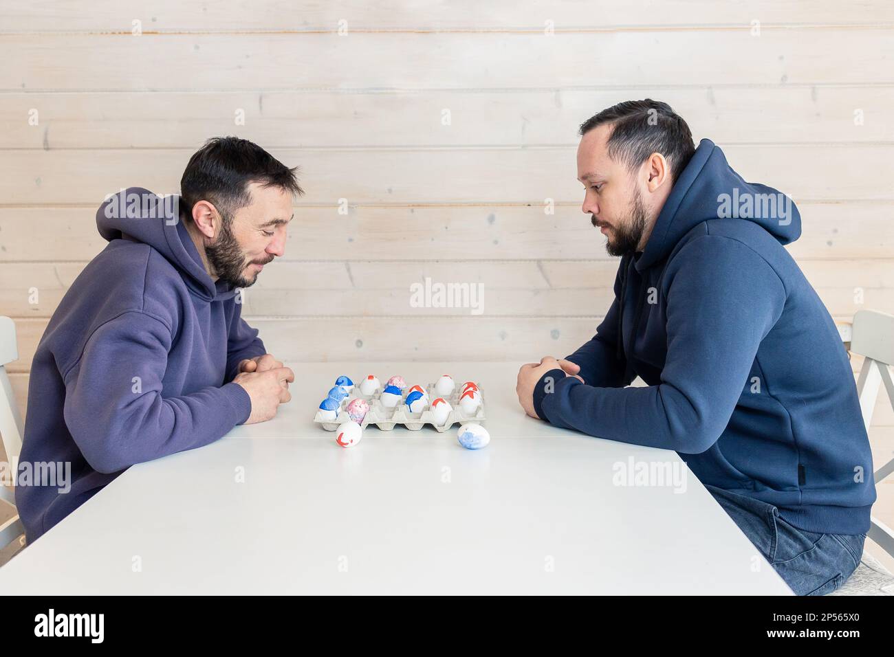 Bearded men play chess with Easter eggs at white table. Creative ideas for unusual chess. Colorful painted egg figures. High quality photo Stock Photo