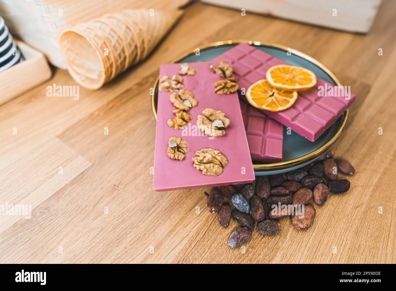 Various ruby pink chocolate bars with nuts, dried orange slices and toasted cacao beans on plate. Wooden table. High quality photo Stock Photo