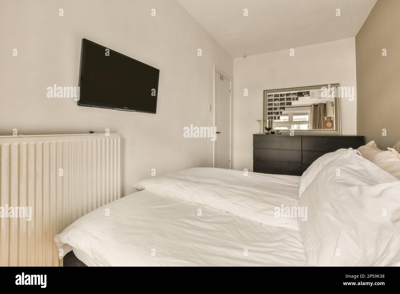 a bedroom with a tv on the wall and bed in the fore - image was taken from an actual photograph Stock Photo