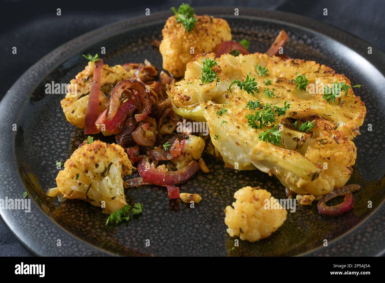 Baked spicy cauliflower slices with red onions on a black plate, healthy vegetable dish for low carb diet, close up shot, copy space, selected focus, Stock Photo