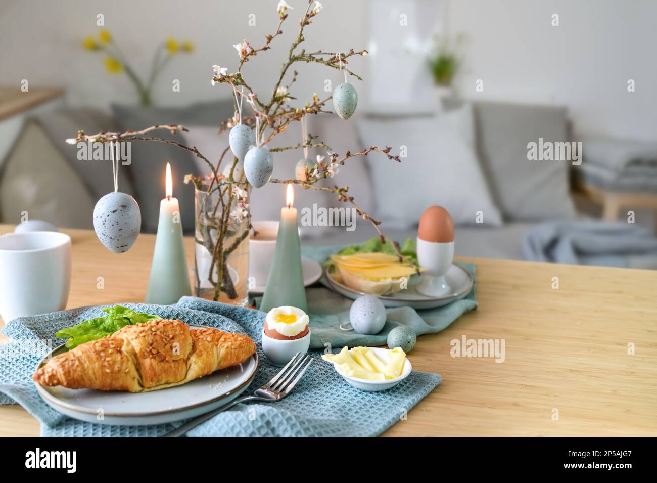 Breakfast table with boiled egg, croissant and pastel turquoise Easter decoration in a small living room, copy space, selected focus, narrow depth of Stock Photo