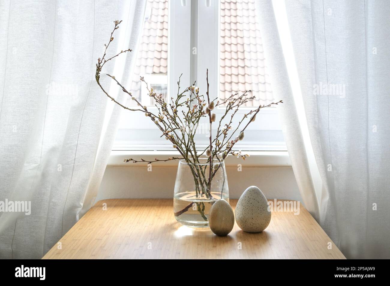 Pussy willow catkins and flowering branches in a glass vase and artificial eggs as Easter decoration on a table at the window in an old town city flat Stock Photo
