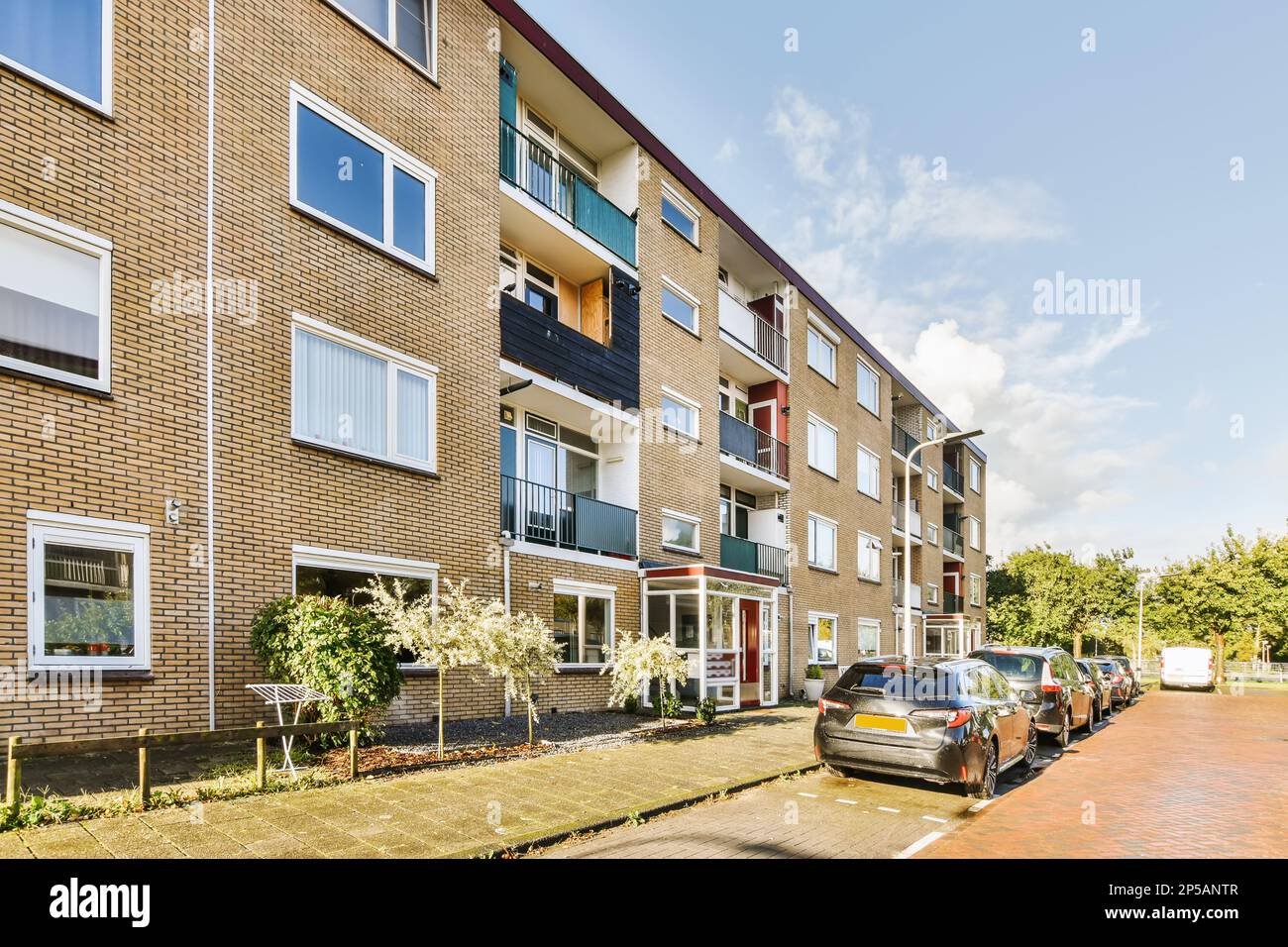 an apartment complex with cars parked on the street and trees in the ...