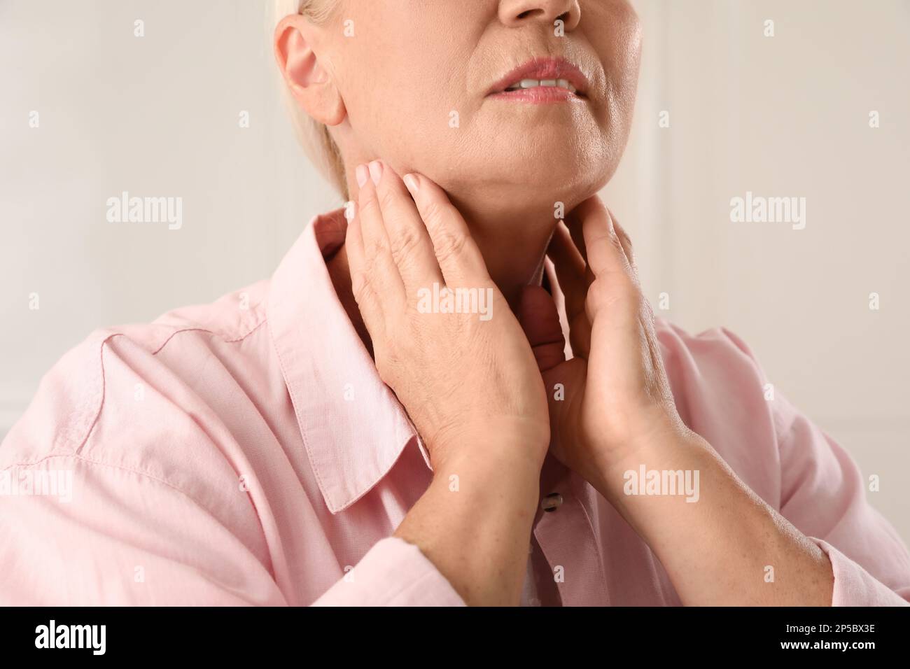 Mature woman doing thyroid self examination on light background, closeup Stock Photo